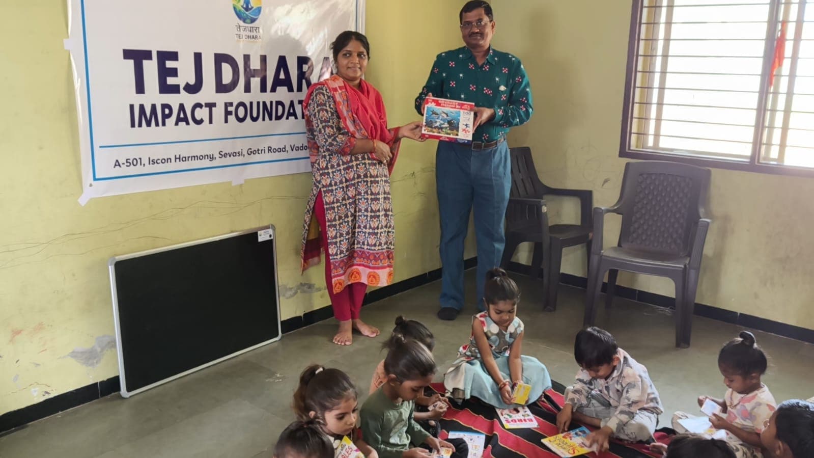 Tej Dhara volunteer handing over a 100-piece puzzle book under the foundation banner