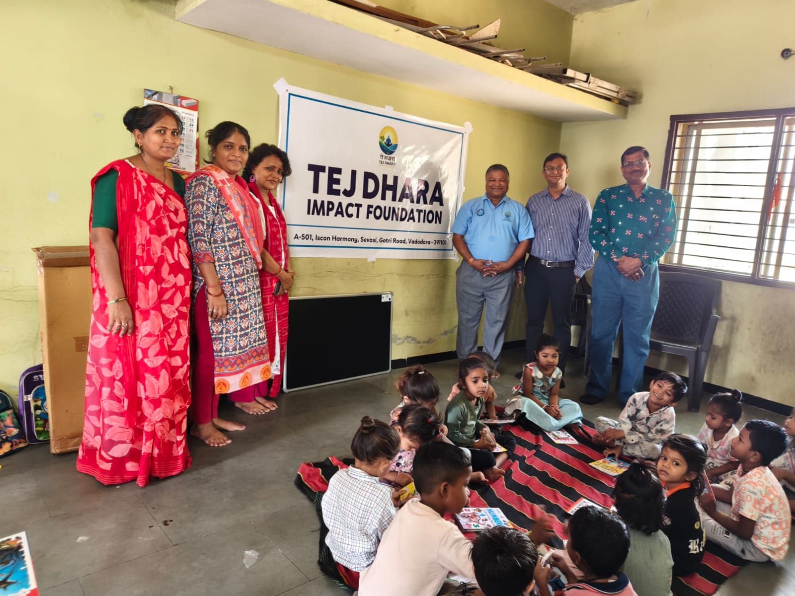 The Tej Dhara volunteer team standing with the Anganwadi children in front of the foundation banner
