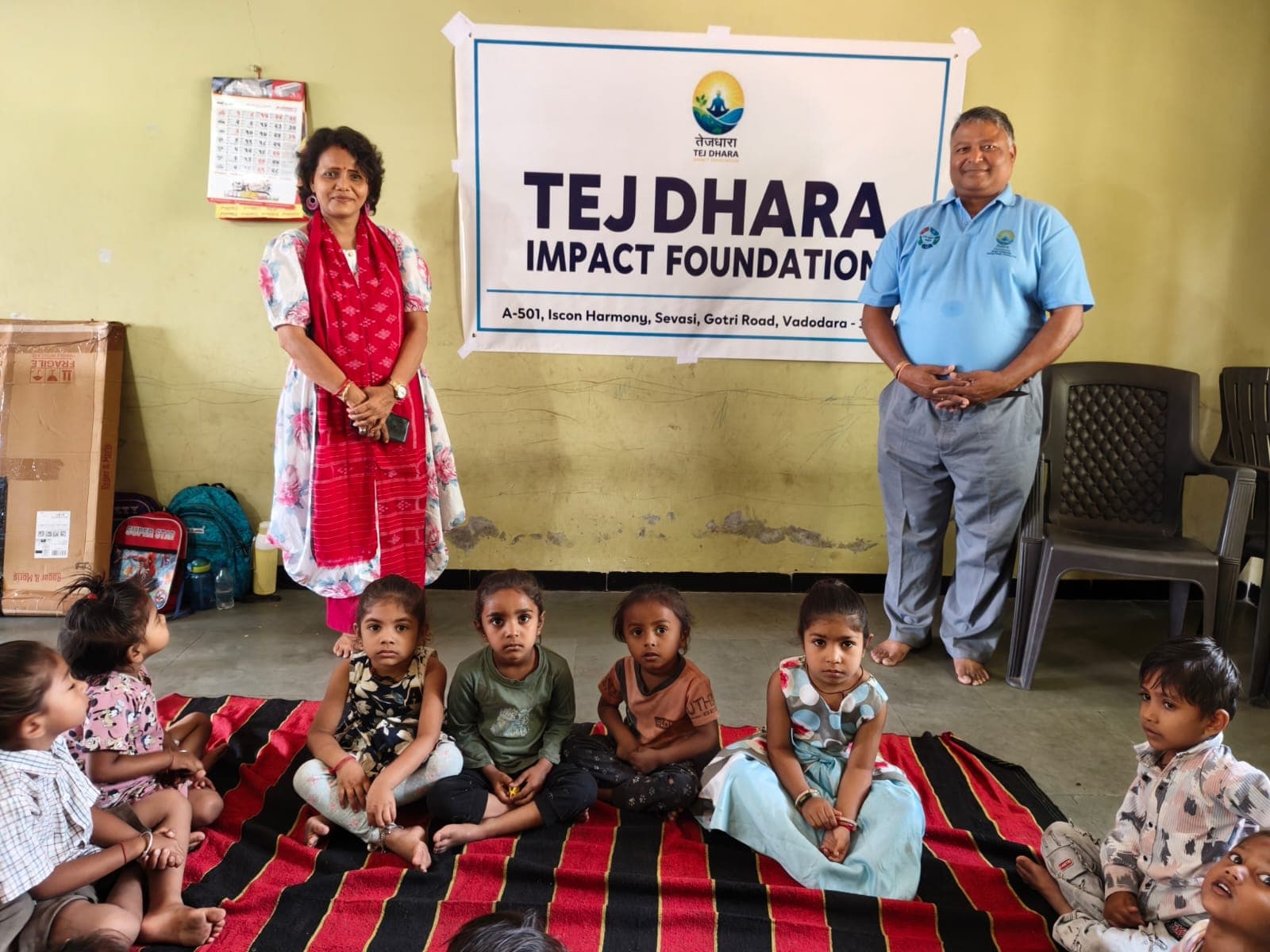 Founders standing with a row of Anganwadi children sitting on a striped floor mat
